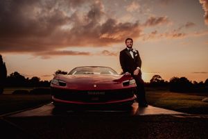 Dramatic sunset portrait with red Ferrari sports car at luxury wedding.