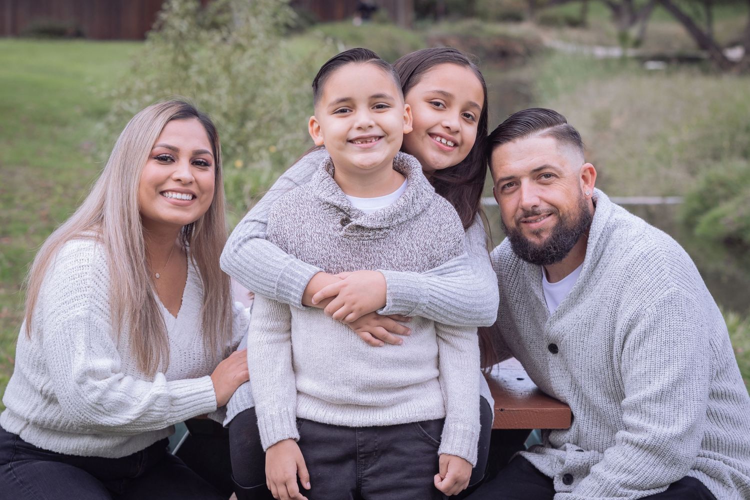Family of four poses outdoors wearing coordinated gray sweaters.
