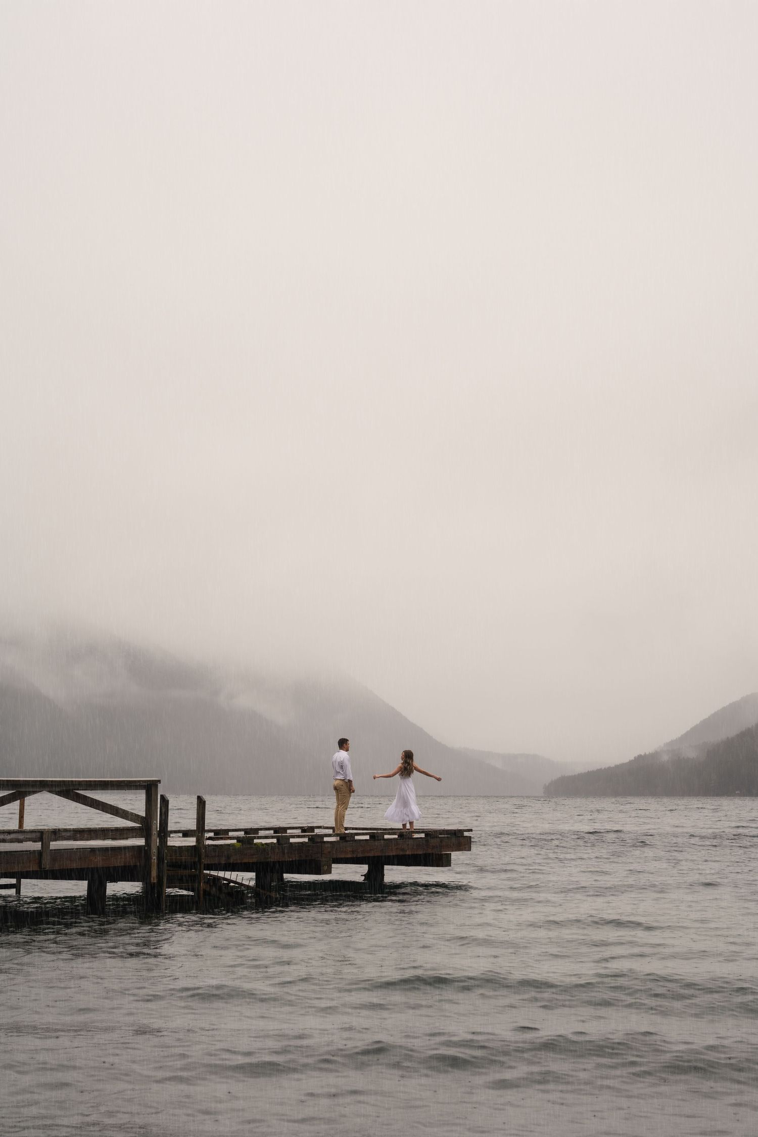 A couple shares a romantic moment on a wooden dock overlooking a misty mountain lake.