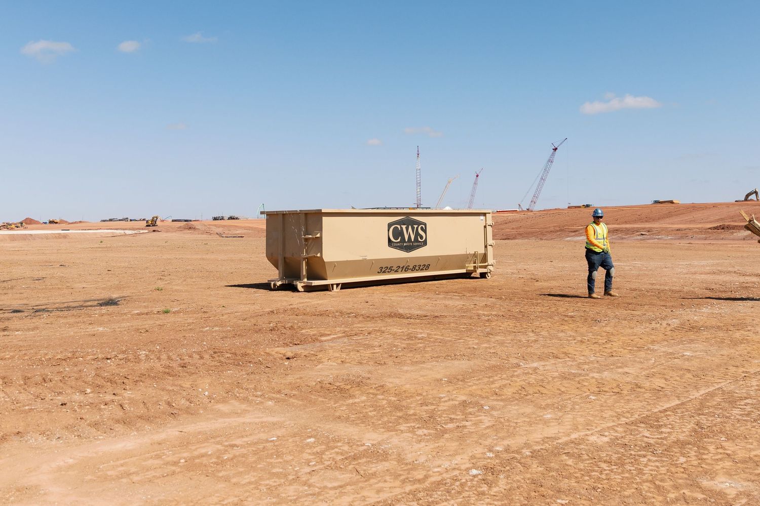 A shipping container sits in a desert landscape with a worker in high-vis gear nearby.