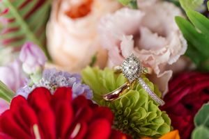 Diamond engagement ring and gold wedding band resting on colorful bridal bouquet with roses.