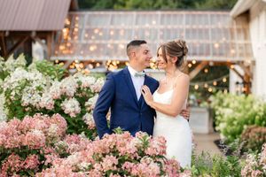 Bride and groom smiling among pink hydrangeas with string lights at elegant garden wedding at The Promise Gardens of the Adirondacks.