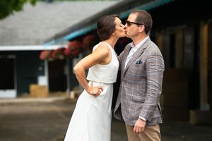 Cherie DeVaux in white gown and David Ingordo in plaid blazer kiss outside at Fasig-Tipton in Saratoga Springs, NY during wedding party.