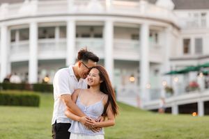 Happy couple embracing and laughing in front of a grand white colonial building on a green lawn The Sagamore Resort on Lake George, NY.