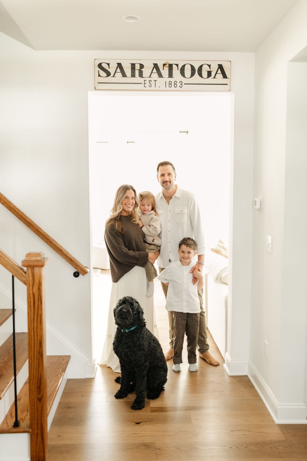 Happy family with two children and black dog posing under Saratoga sign in bright home entryway.