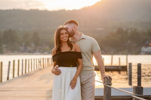 Couple embracing on a wooden pier at golden sunset with mountains and water in the background The Sagamore Resort on Lake George, NY..