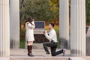 Man proposing to woman on one knee in outdoor columned monument area in Congress Park in Saratoga Springs, NY during Fall.