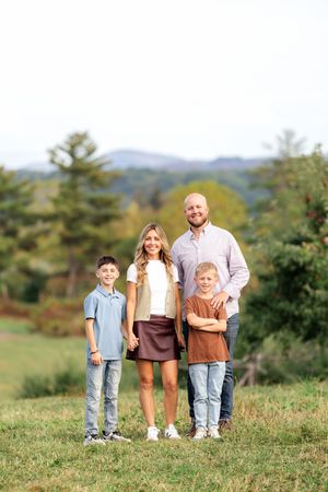 Family of four posing outdoors with mountain and evergreen tree backdrop in fall.