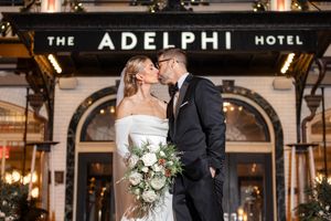 Bride and groom sharing a kiss outside The Adelphi Hotel entrance adorned with twinkling holiday lights in Downtown Saratoga.