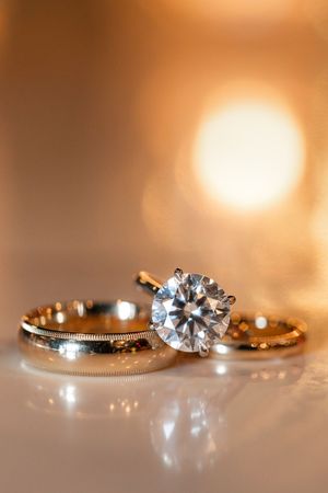 Close-up of a stunning round diamond solitaire engagement ring alongside two gold wedding bands with warm bokeh.