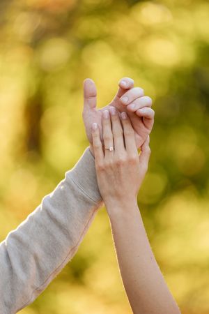 Close-up of couple holding hands showing engagement ring with bokeh autumn background.