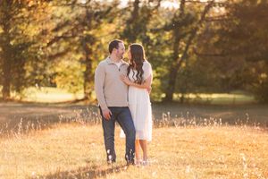 Couple gazing at each other in sun-drenched autumn meadow with golden tree backdrop.