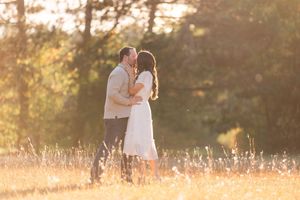 Couple sharing romantic kiss in golden sunlit meadow surrounded by autumn trees.