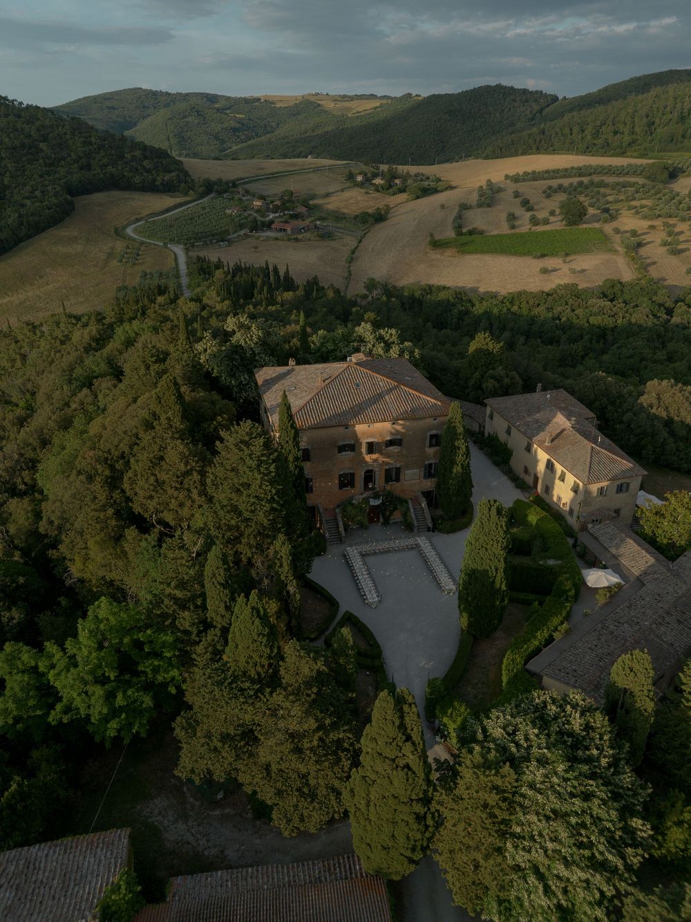 Aerial view of a Tuscan villa surrounded by lush trees and rolling hills in the Italian countryside.