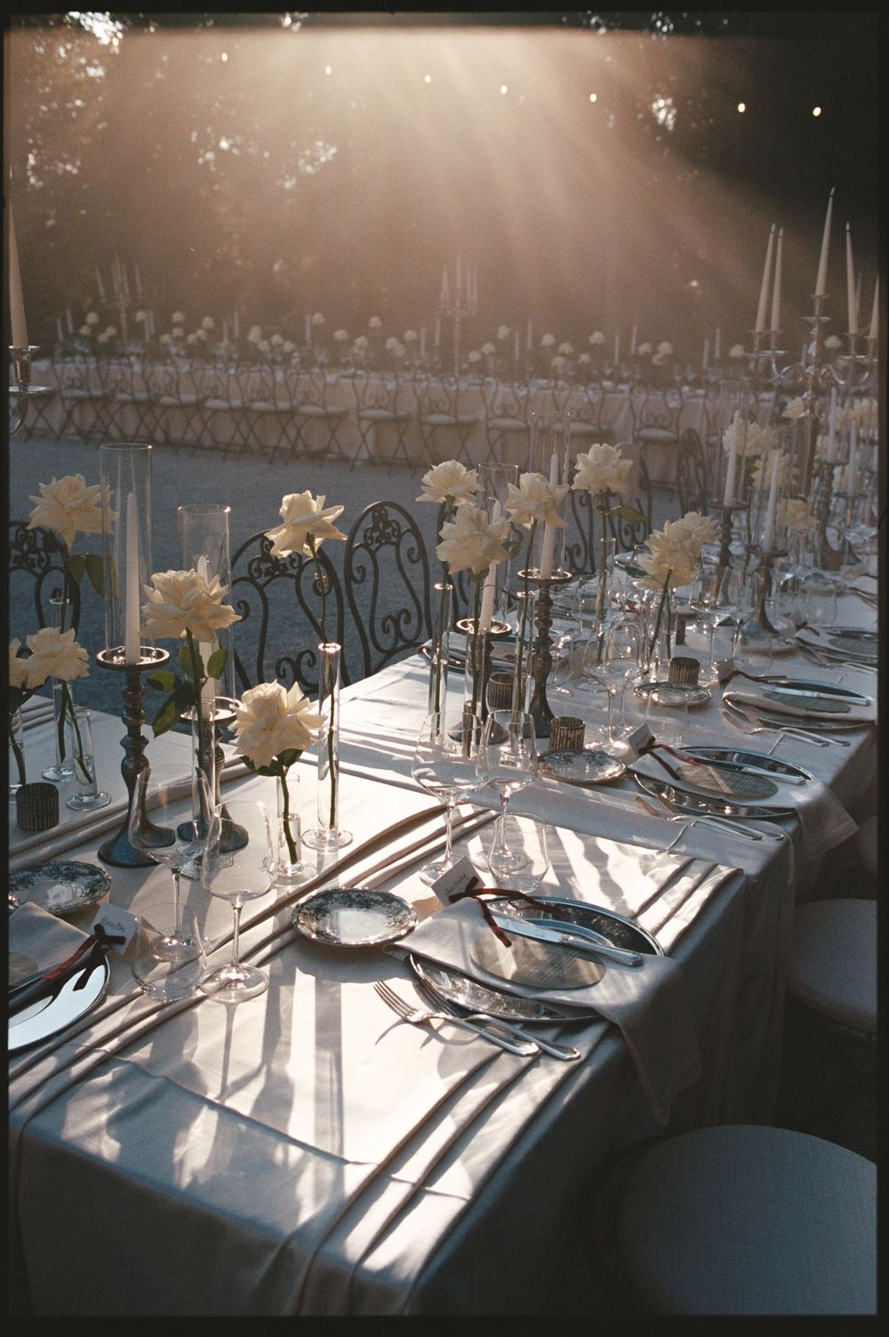 Sunlit wedding reception table with white floral centerpieces, crystal glassware, and elegant silver candlesticks.