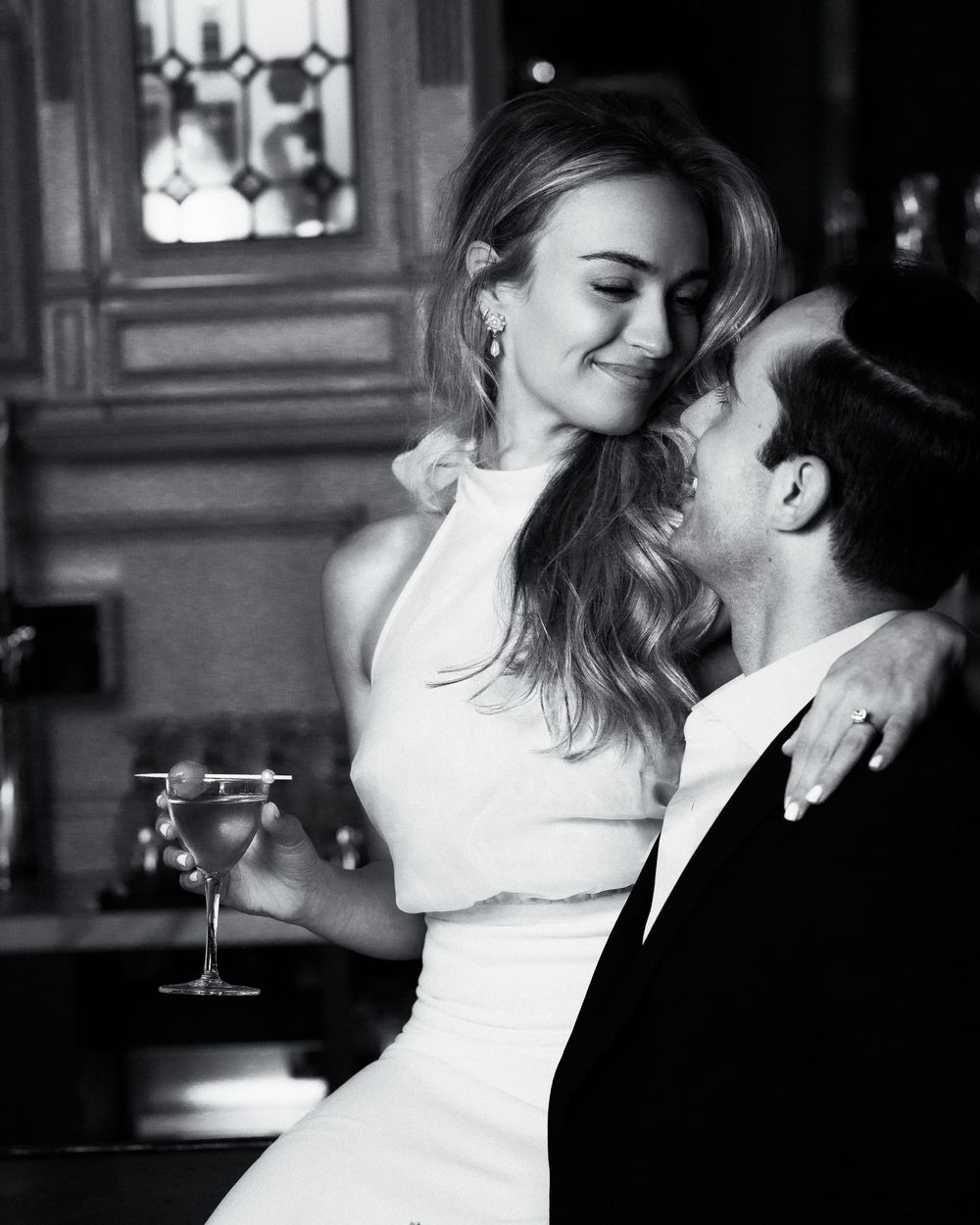 Black and white wedding portrait of a smiling bride in her groom’s arms, elegant and cinematic.