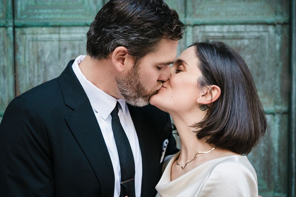Photo of a bride and groom sharing a romantic kiss in front of a rustic green door, capturing love and intimacy on their wedding day.