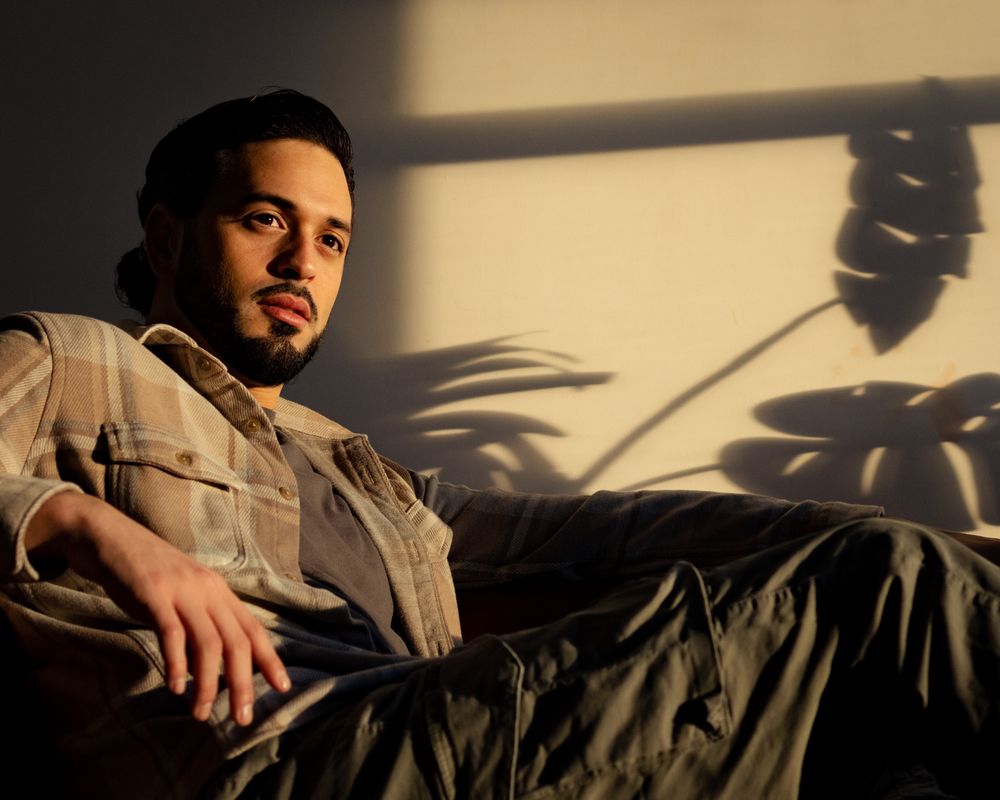 Robbie reclined in golden hour light, with palm frond shadows cast dramatically on the wall behind him — quiet, cinematic, effortless.