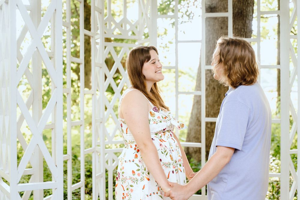 A group in floral dresses and purple shirts pose in front of a white gazebo with sunlight streaming through.