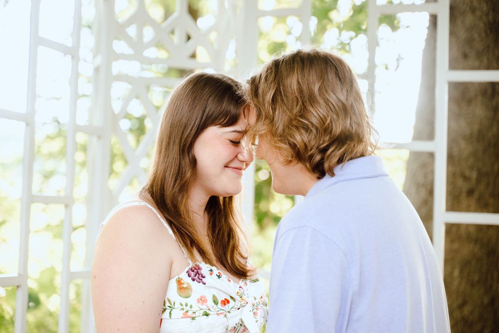 A romantic photo session in a garden shows a couple in white embracing each other in soft natural sunlight.