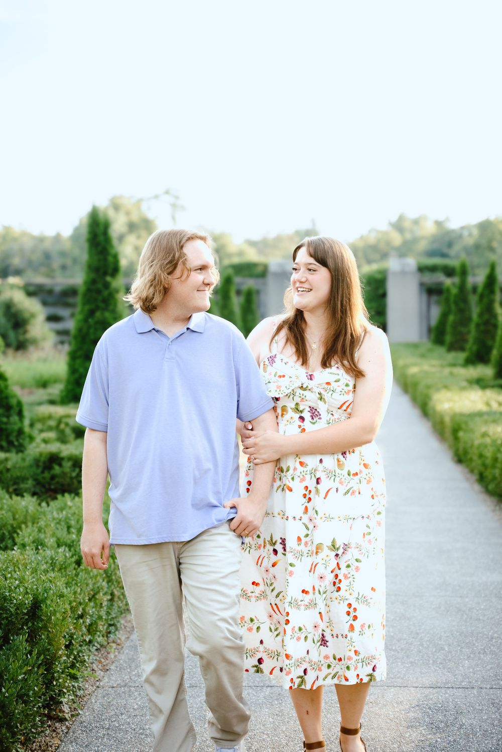 Couple walking and laughing together on a garden path during a sunny summer engagement photo session.