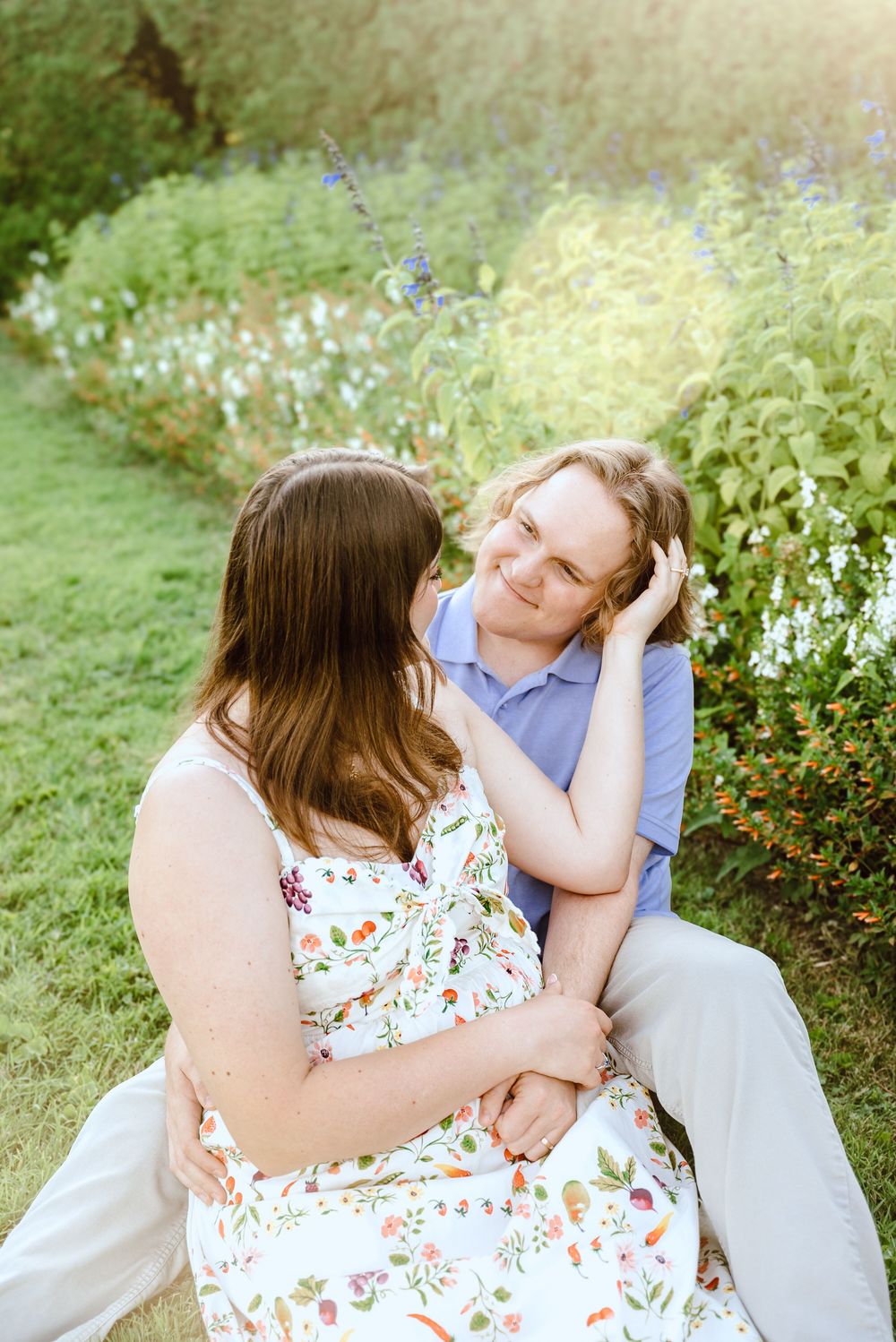 Couple sitting together in a garden with white flowers and greenery on a sunny afternoon.