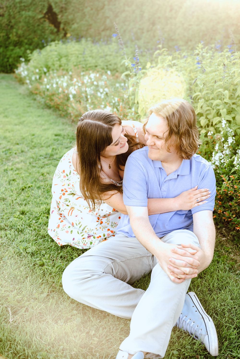 A loving couple relaxes together in a meadow filled with small white flowers on a sunny spring day.