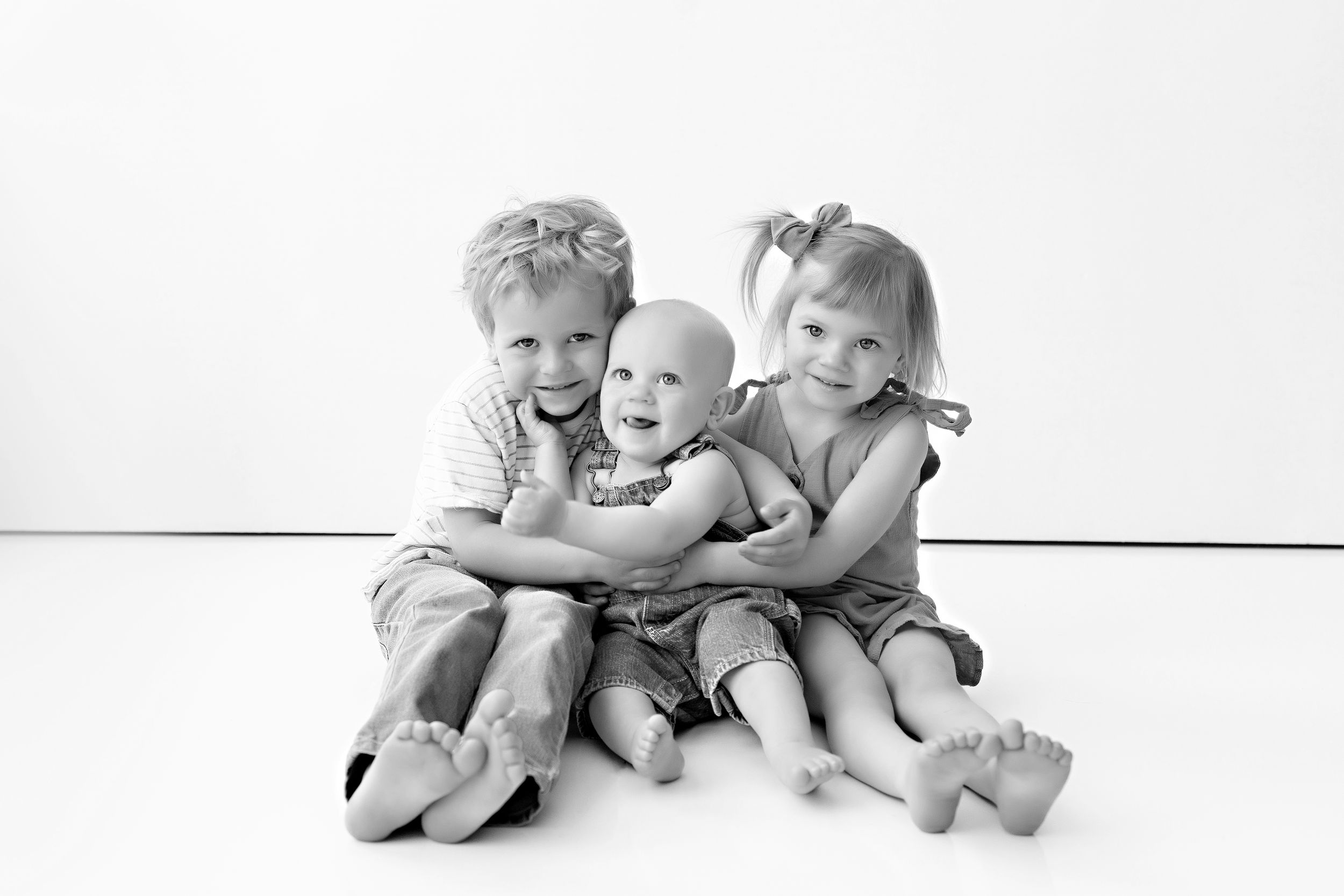 Three adorable siblings positioned in hugging pose against white background. Sibling photography.