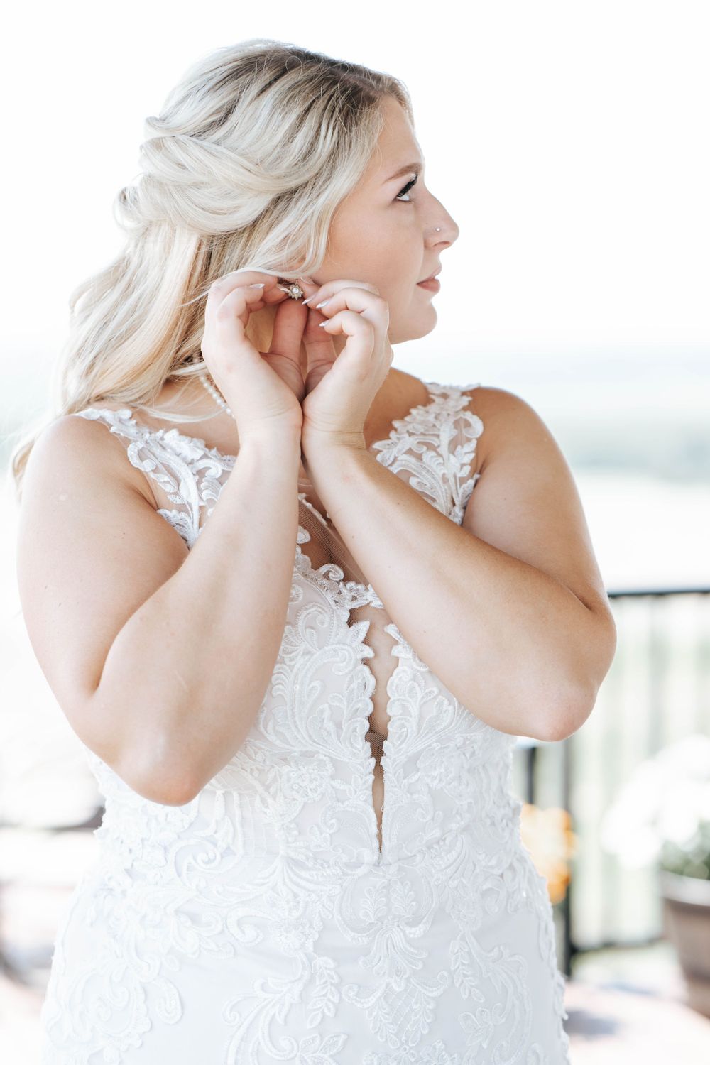 Close-up of someone wearing an elegant white lace wedding dress adjusting earrings.