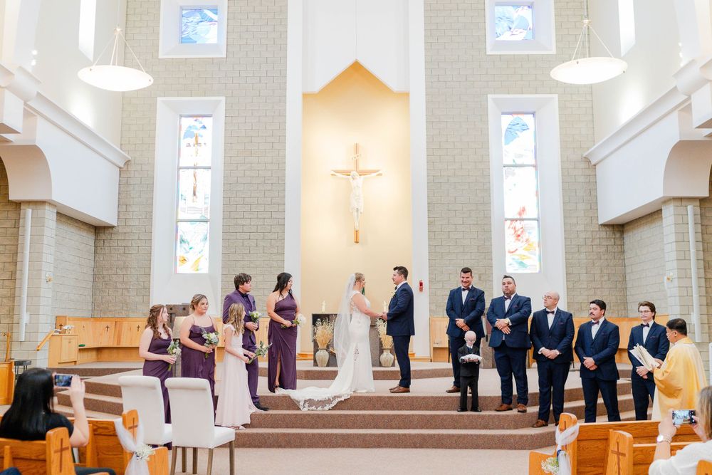 A traditional church wedding ceremony with bridesmaids in purple and groomsmen in navy suits at the altar.