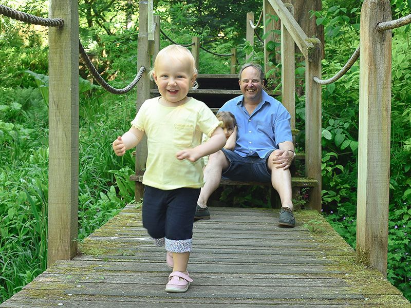 A father and his daughter enjoy a playful moment on a bridge, captured in a natural family photography session by Abigail's studio.
