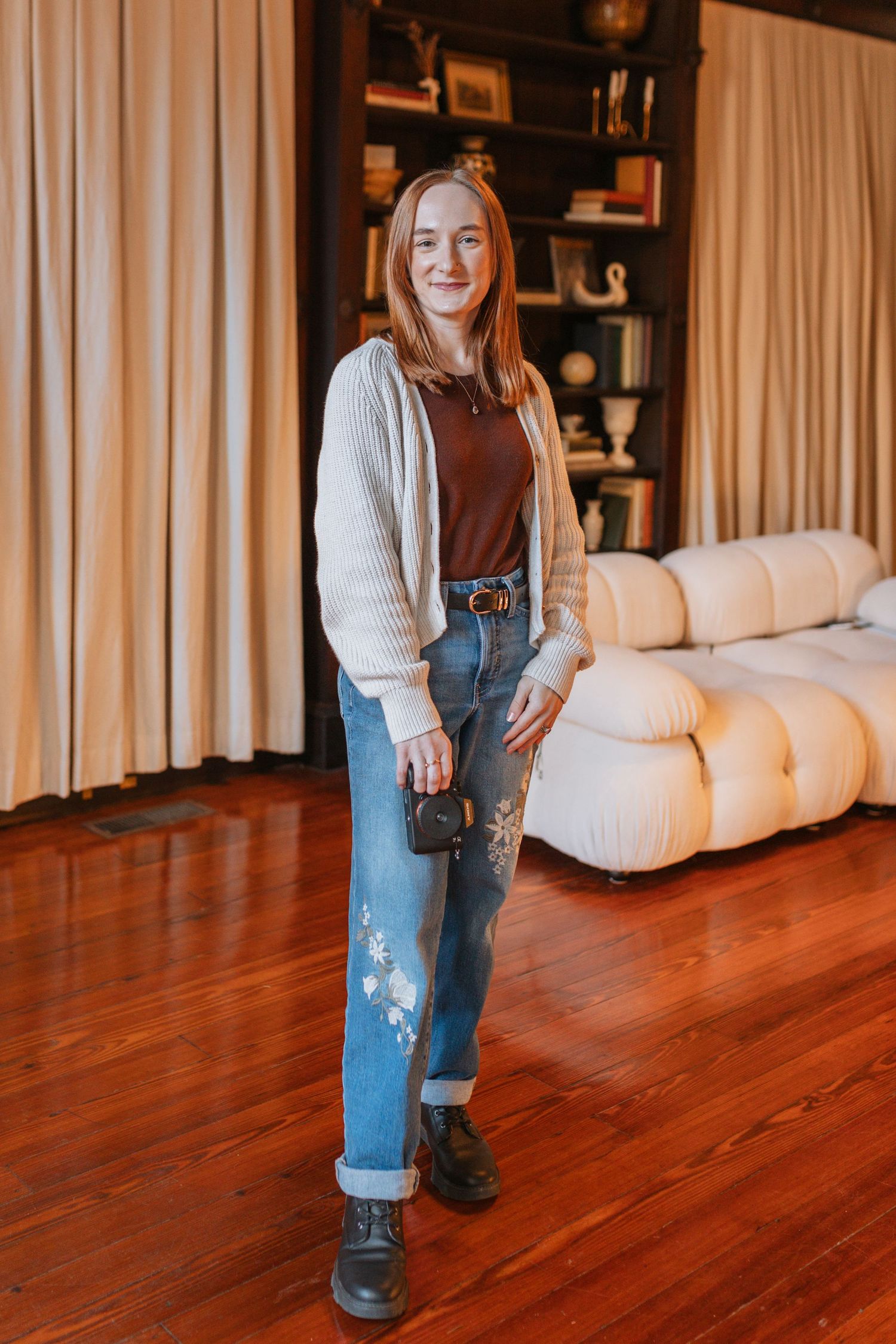 Person wearing denim overalls and white sweater standing on hardwood floor.