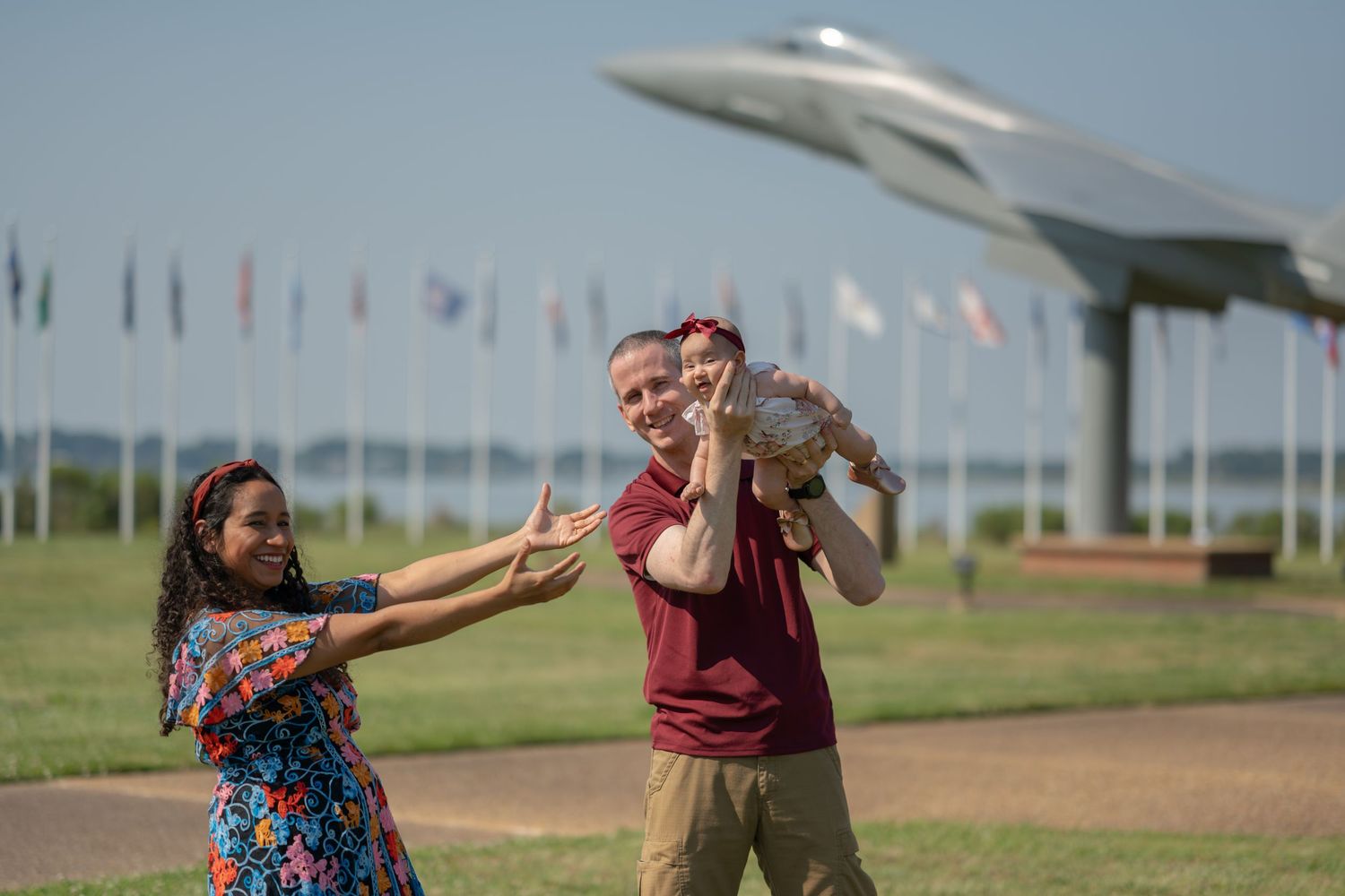 A family plays together in front of rows of flags and a military aircraft display on a sunny day.