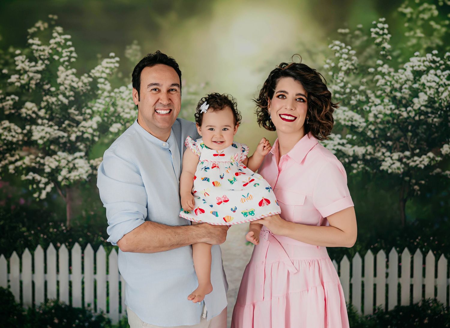 Niña de un año con sus padres en un entorno natural con flores y árboles durante una sesión de fotos familiar