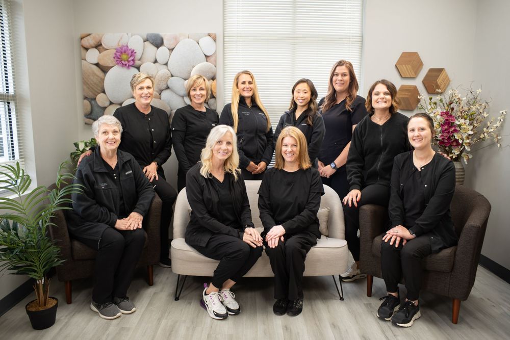 Healthcare team in black attire poses together on couch in modern office setting. Quad Cities Business Headshot Photography