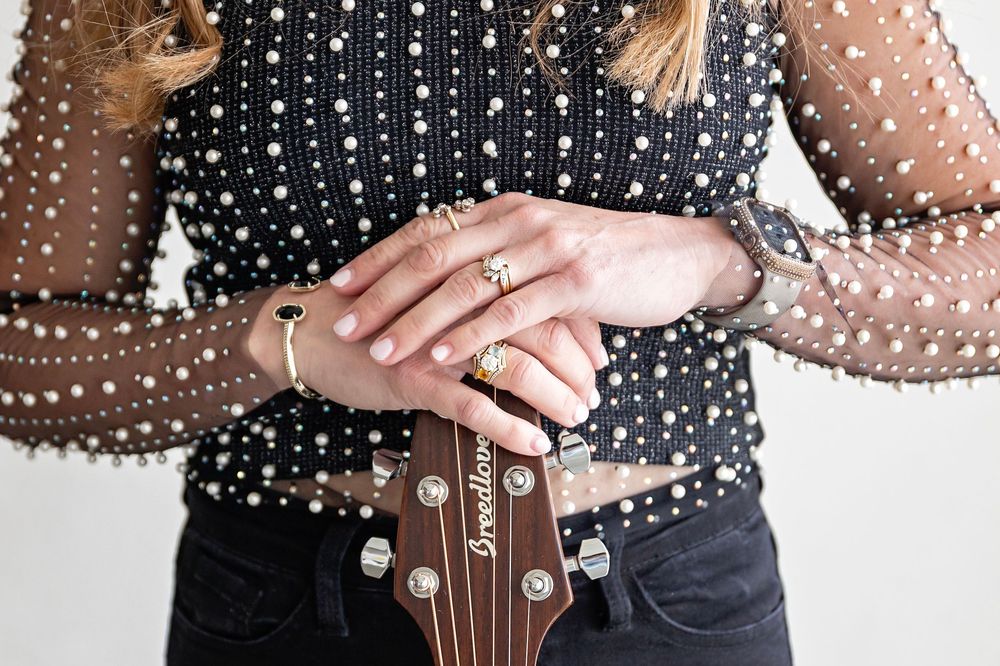 Close-up of hands with rings resting on acoustic guitar neck with pearl inlays.