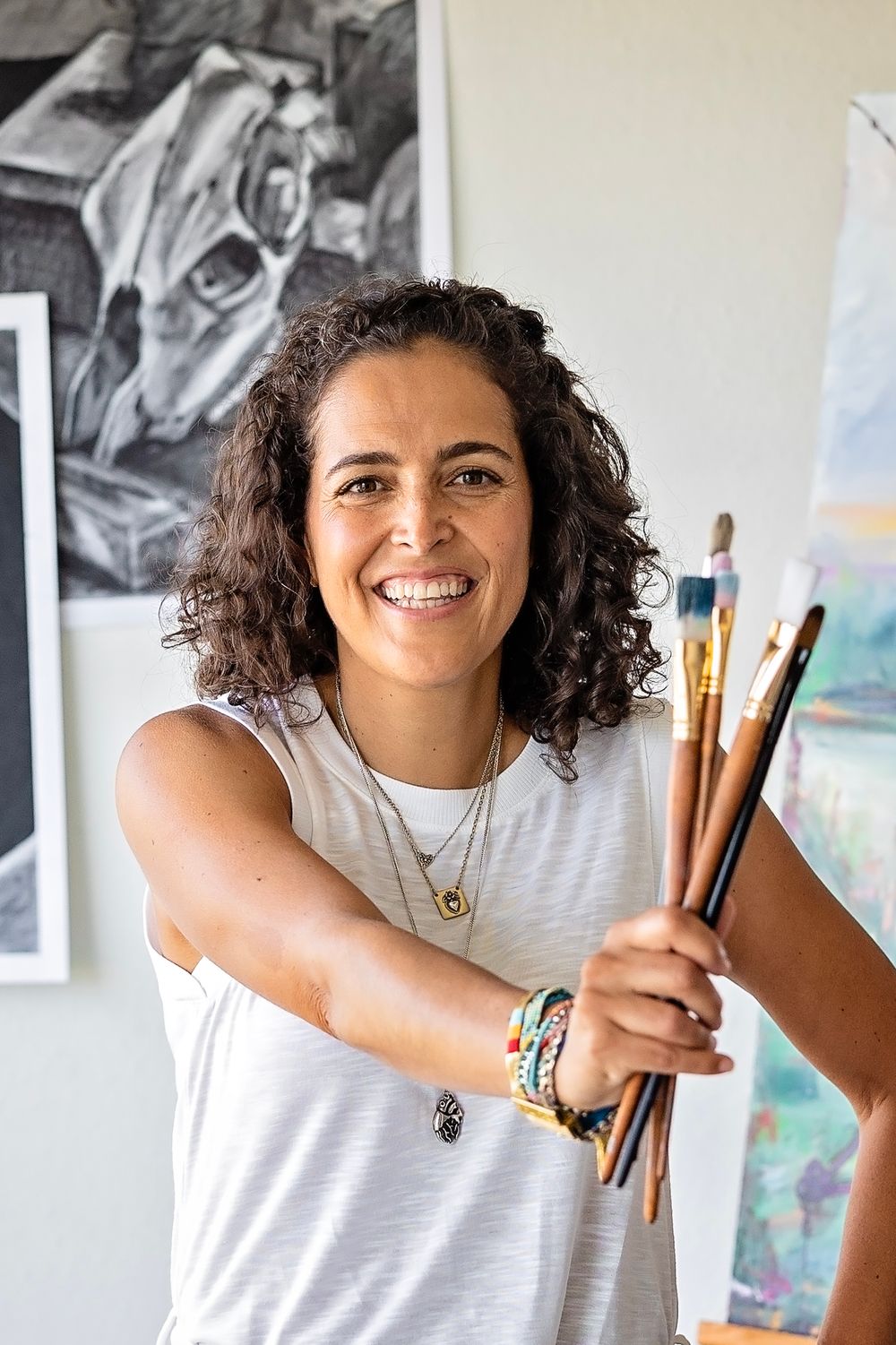 Artist in a white t-shirt holding paintbrushes showcases their creative tools with a warm expression.