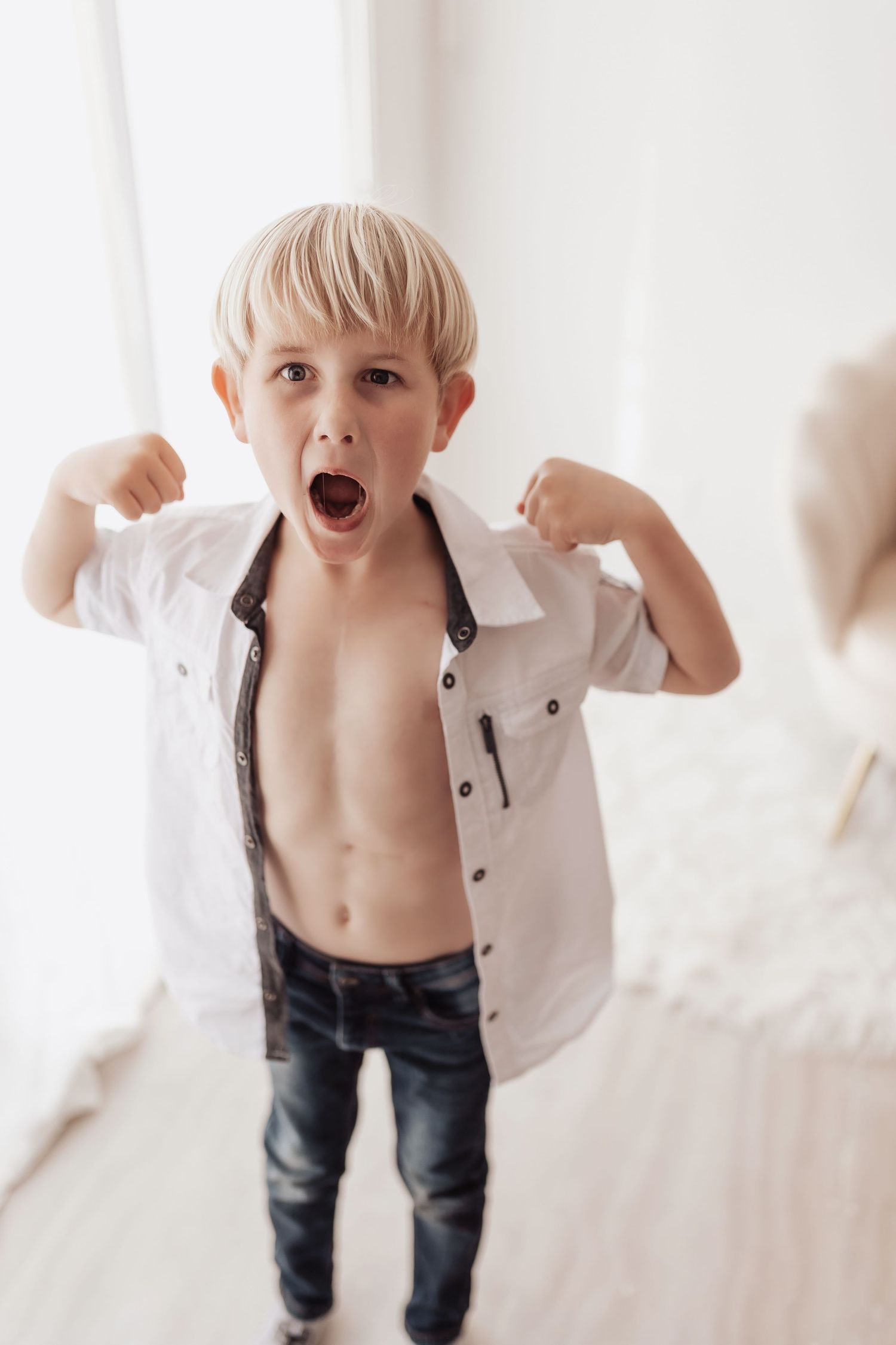 Energetic young child in white shirt and jeans jumps playfully against bright white background.