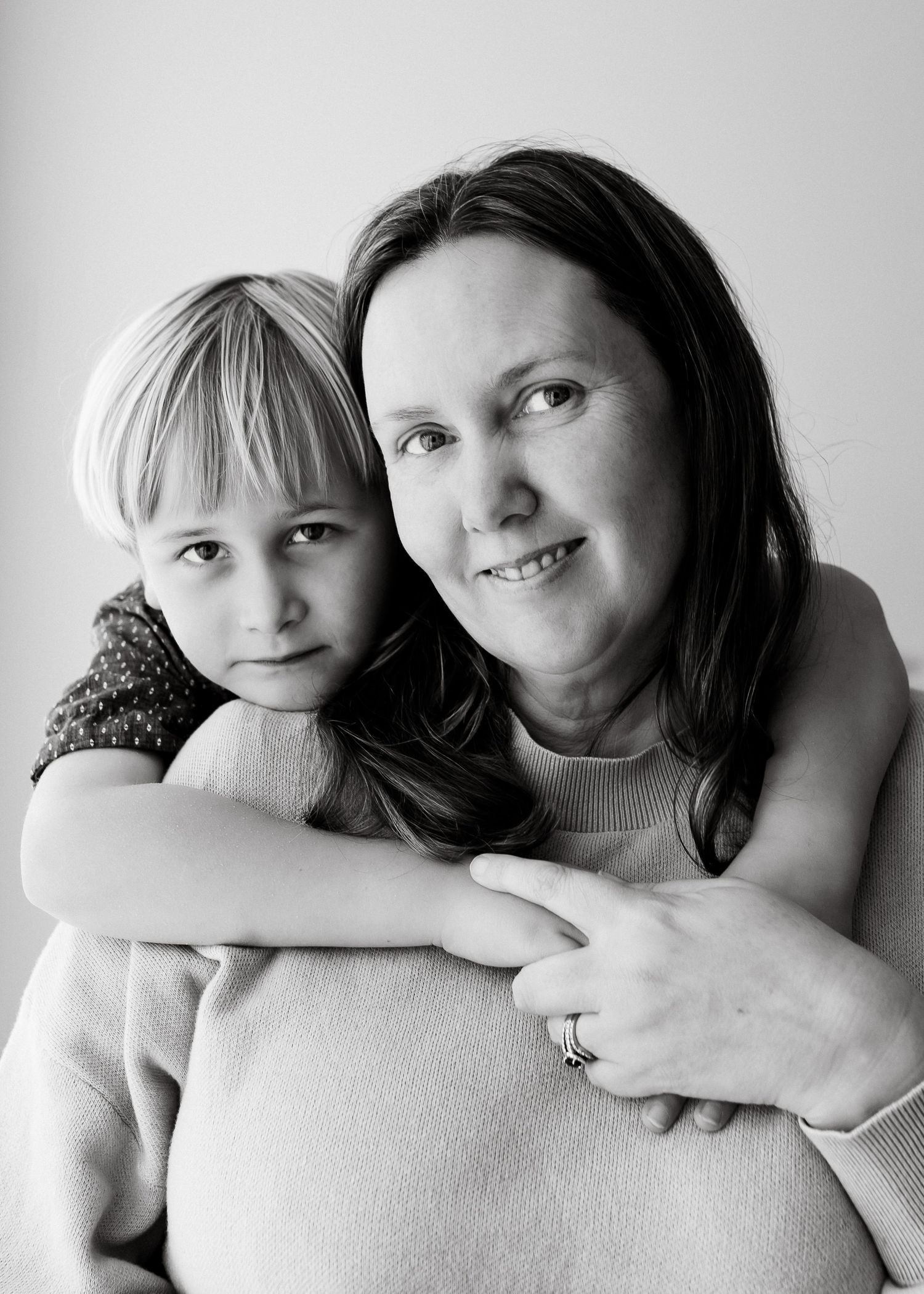 Black and white portrait of a parent and child embracing in a tender moment against a simple background.
