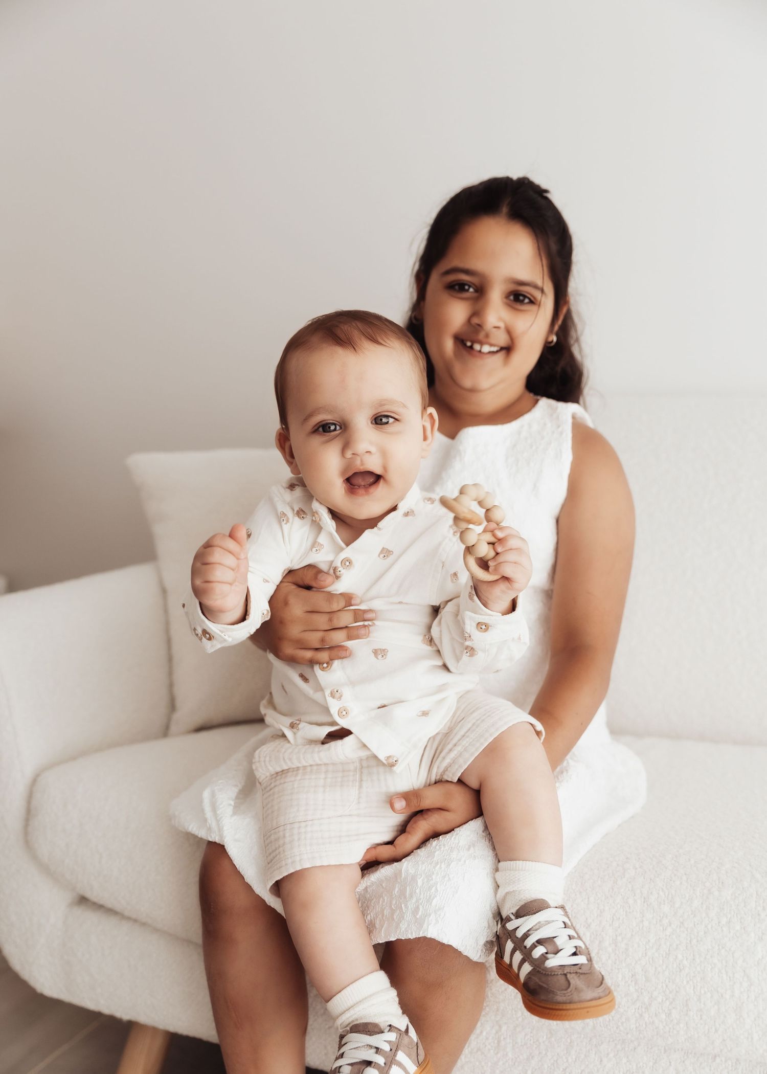 A heartwarming portrait of two people sitting together on a white armchair wearing matching light-colored outfits.
