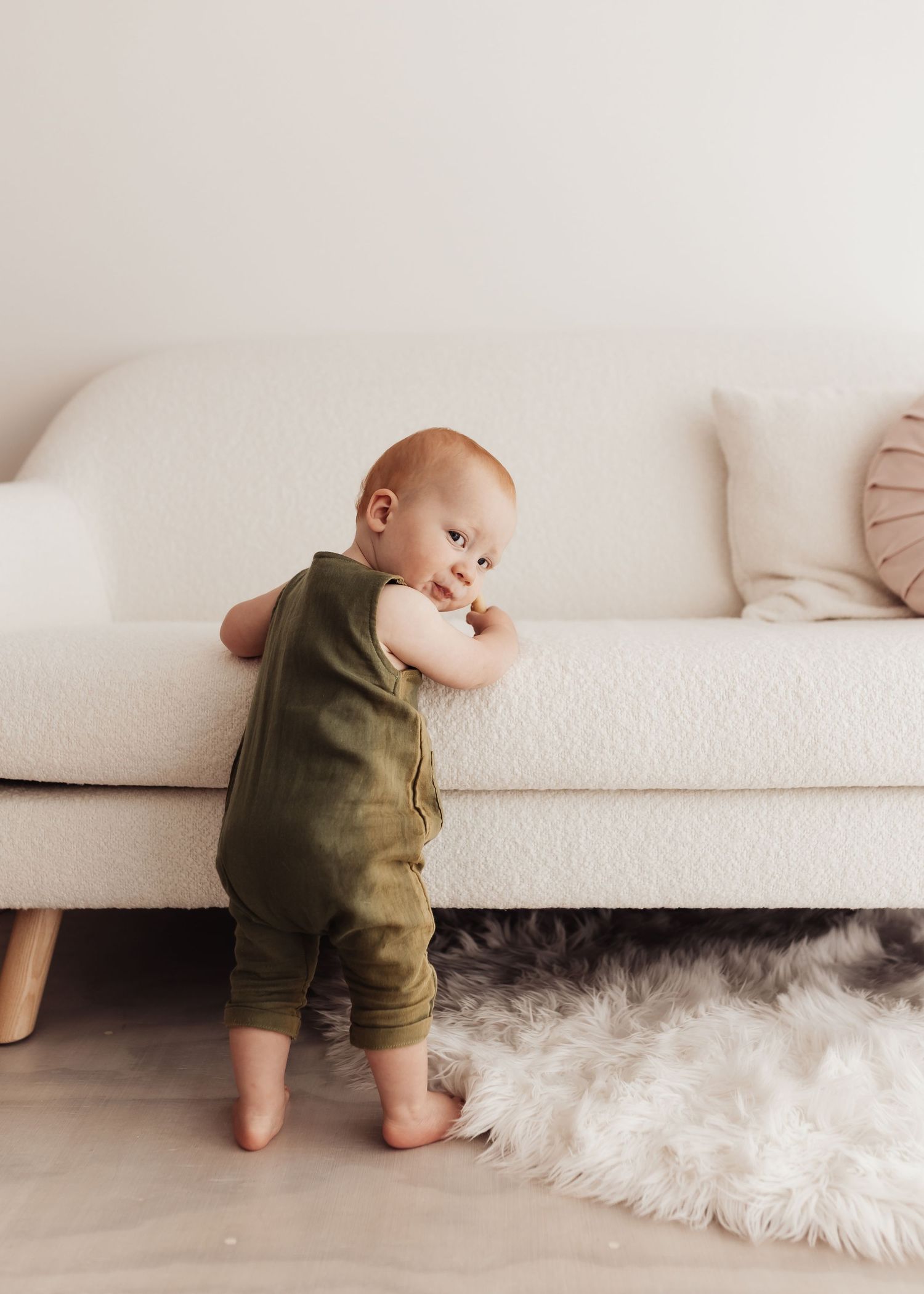 A baby in olive green overalls crawls on a white carpet, shown in a sequence of progressive movements.