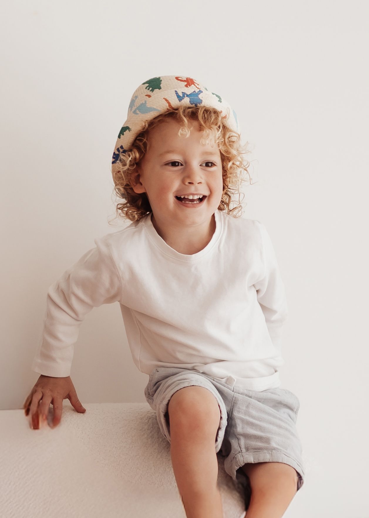 A young child in a white long sleeve shirt and gray shorts plays and jumps around on a light colored floor.