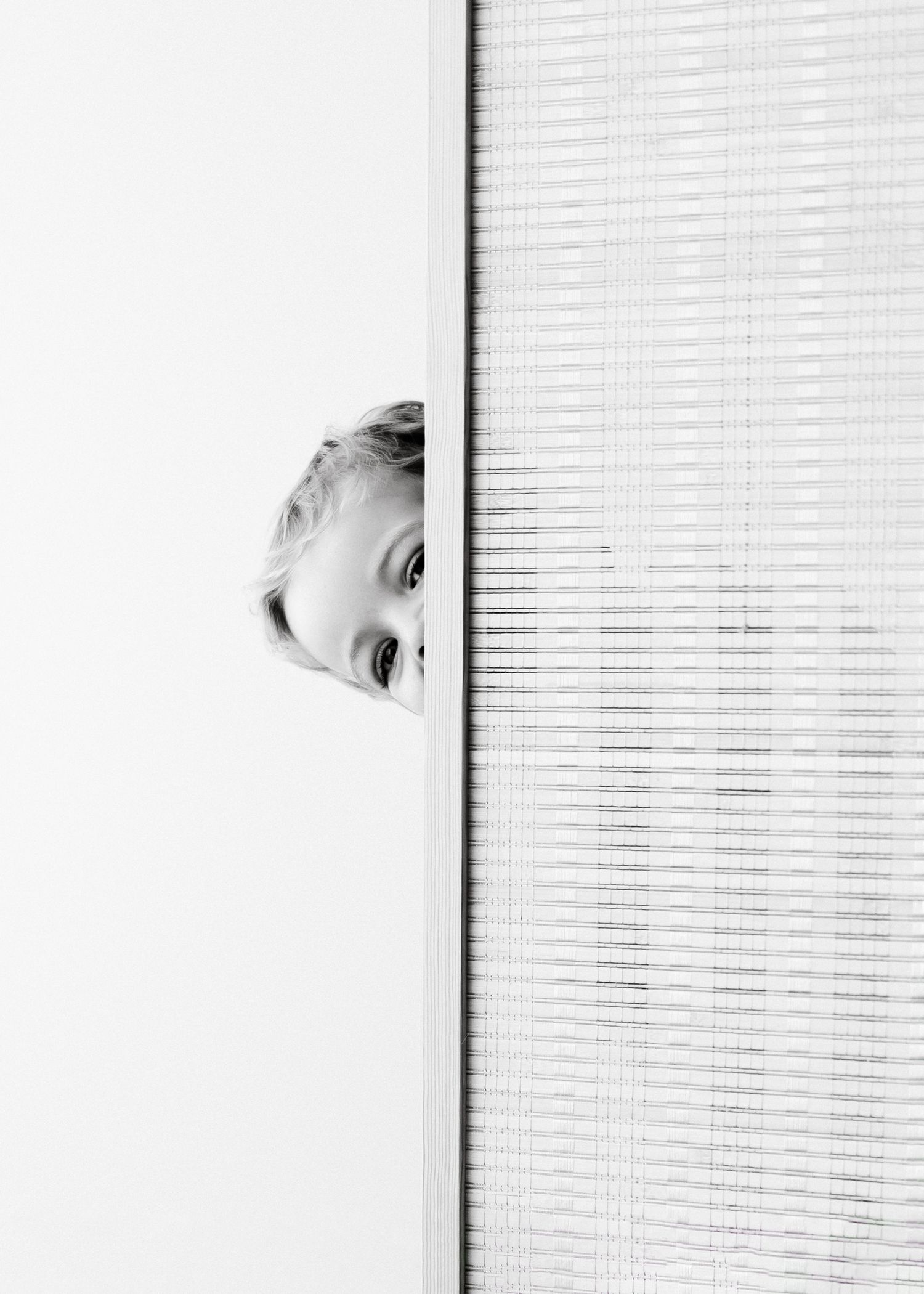 A black and white photo showing a playful peek around a window blind, creating a minimalist composition.