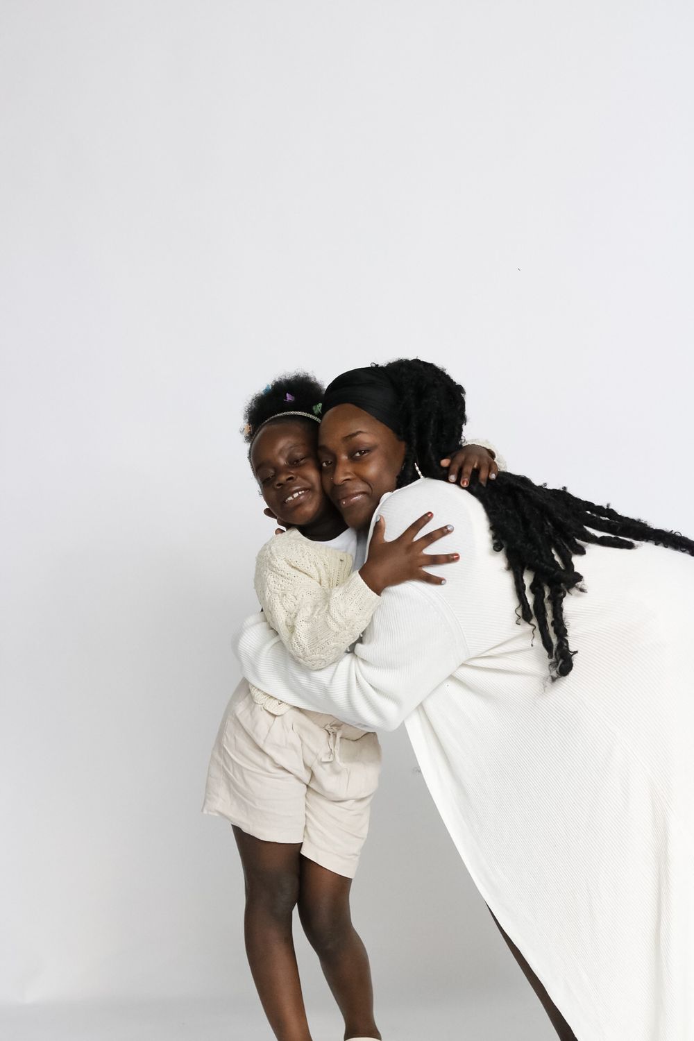 Two people embracing and laughing while wearing white outfits against white background.