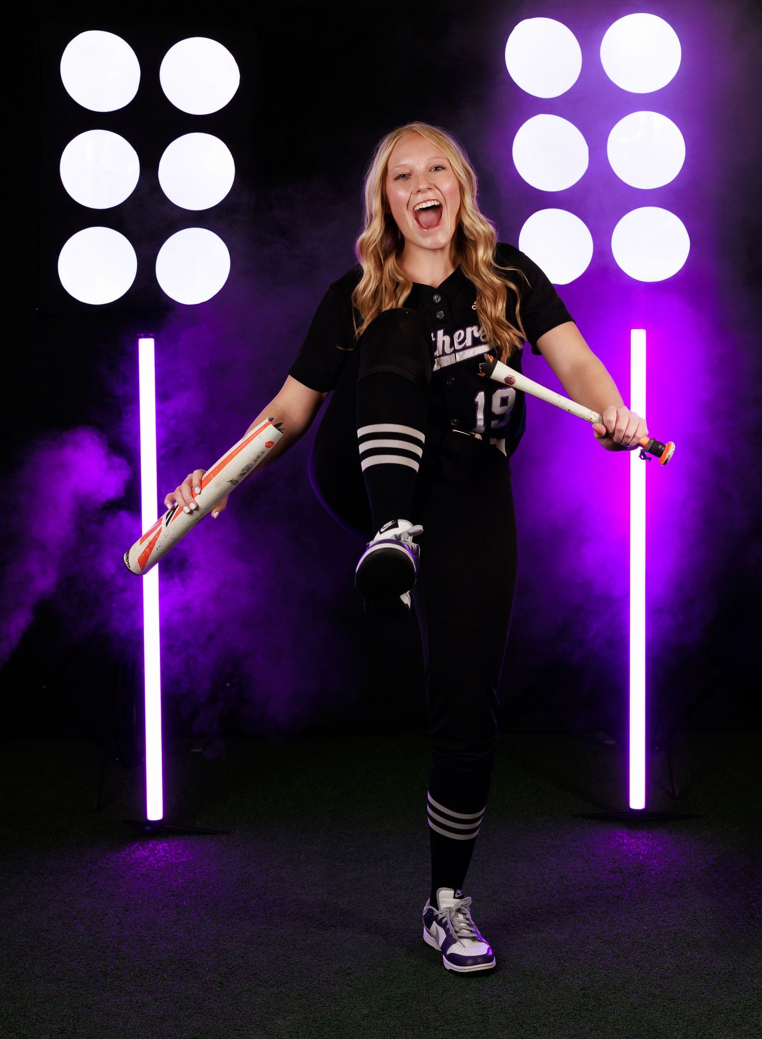 Dancer in black outfit performs energetic moves against purple-lit backdrop with bright spotlights.