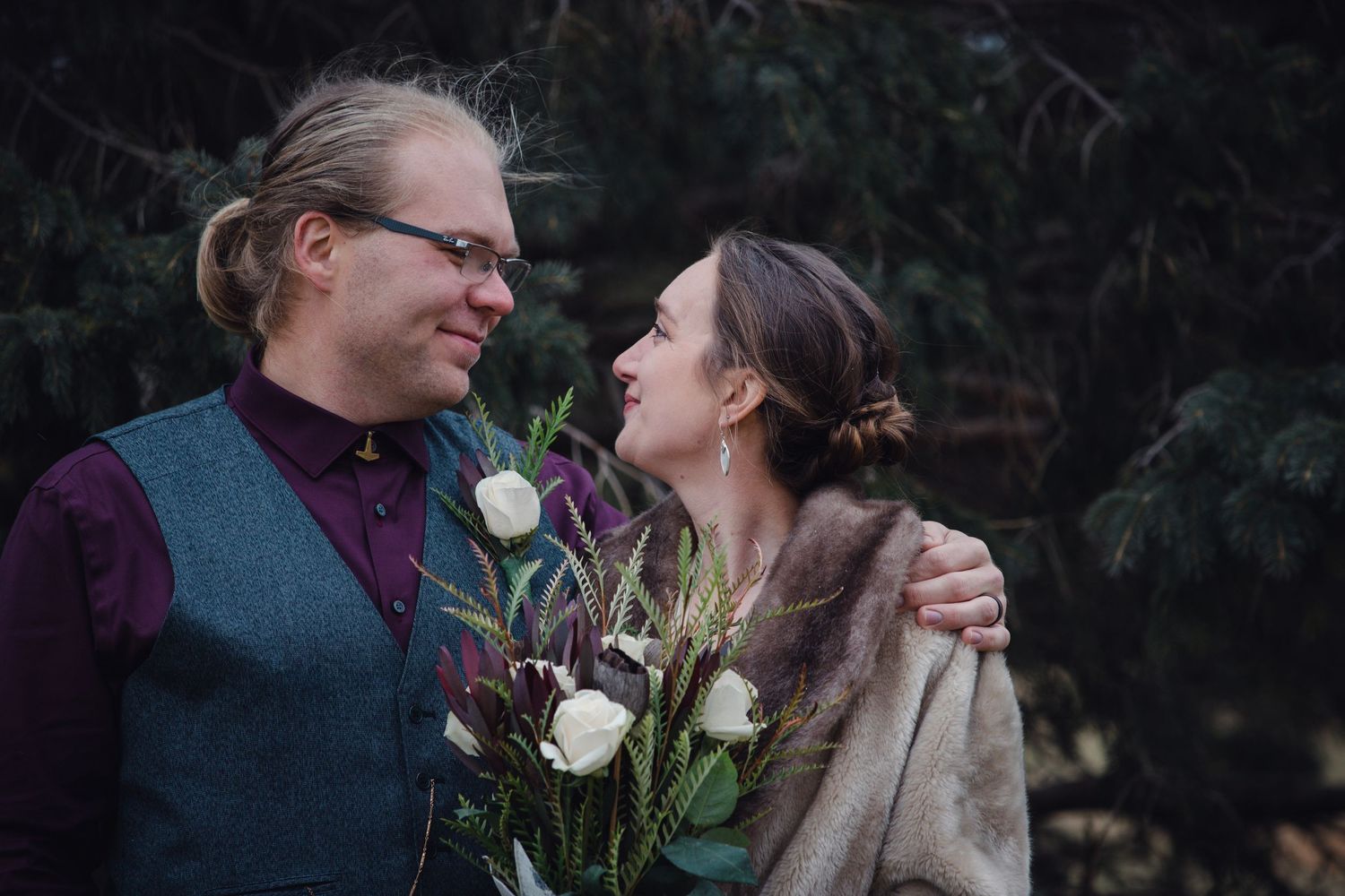 A couple shares a tender moment outdoors while holding white roses on a moody winter evening.