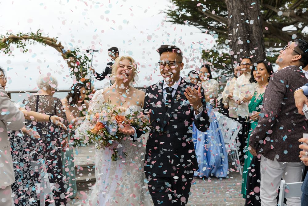 Wedding party celebrates with confetti and laughter during outdoor celebration at scenic waterfront venue.