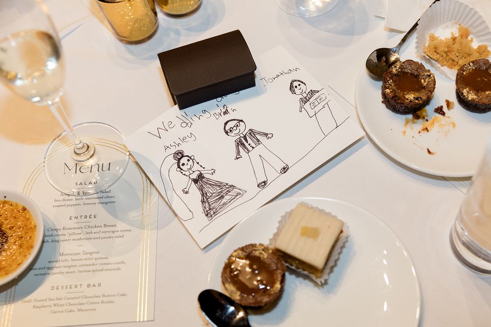 Cute hand-drawn wedding illustrations surrounded by desserts, drinks, and a menu card on a white table setting.