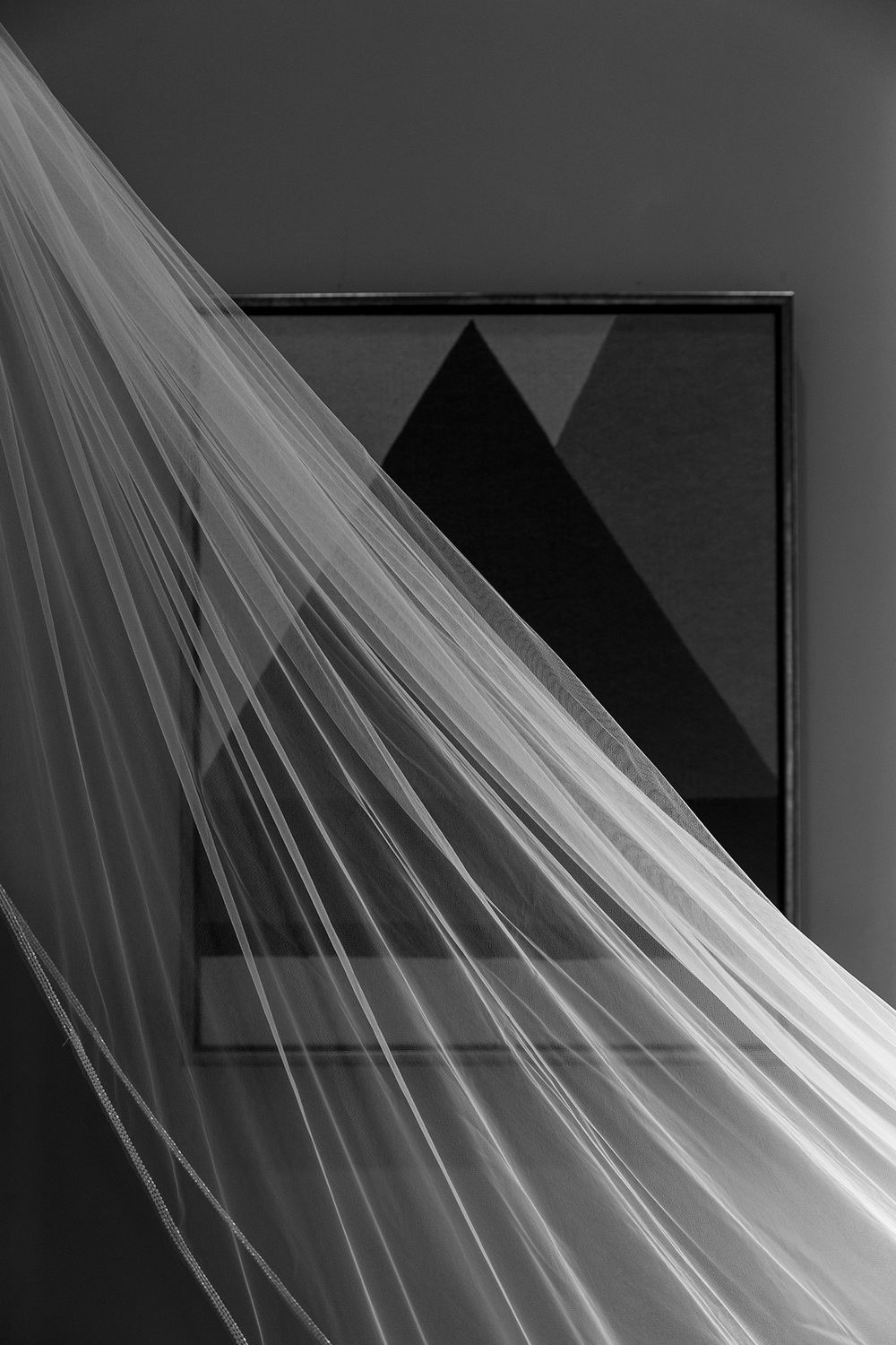A sheer white wedding veil drapes elegantly across a dark framed geometric artwork in black and white.