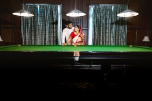 A snooker player lines up a shot on a green felt table under hanging pendant lights.